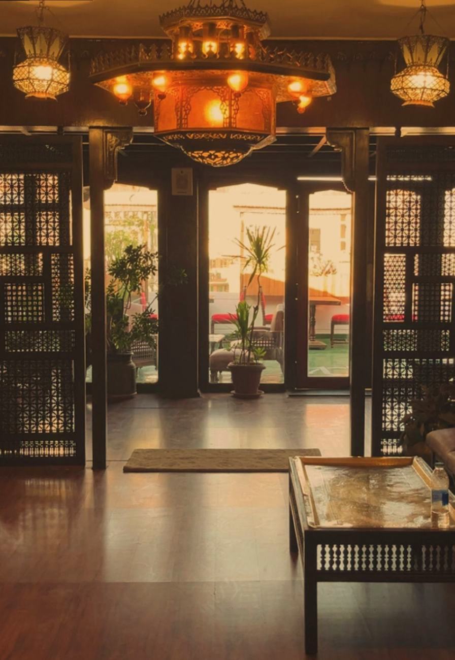 Lantern-lit lounge with mashrabiya screens and doors opening onto the rooftop terrace at sunset