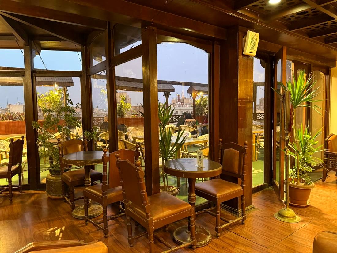 The glazed rooftop lounge, wooden chairs and tables with Downtown rooftops through the windows