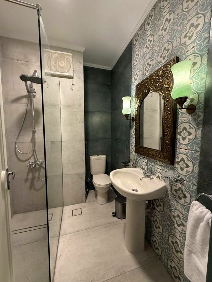Bathroom with a glass rain shower, patterned tiles and an arabesque-framed mirror