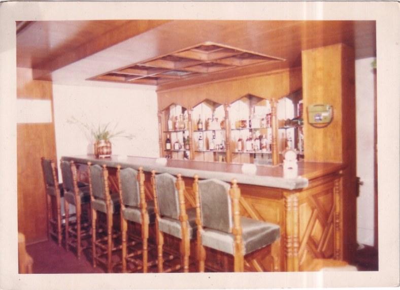 Archive photograph of the bar with arched mirrored shelves and turned-wood stools