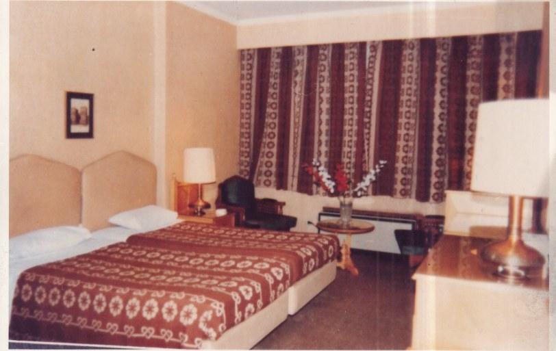 Archive photograph of a guest room with patterned curtains and a woven bedcover